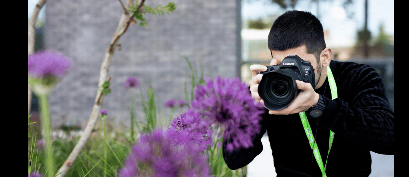 Promotional banner for the level 1 photography course with a picture of a photography student capturing a photograph of vibrant purple flowers in a natural setting.